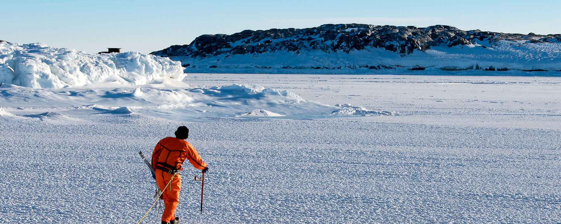 Expeditioner in a dry suit and harness tests the sea ice thickness