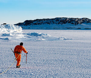 Expeditioner in a dry suit and harness tests the sea ice thickness
