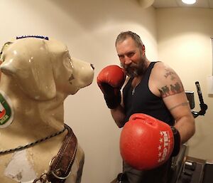 A bearded and tattooed male expeditioner, complete with large boxing gloves, pretends to box with a plastic guide dog