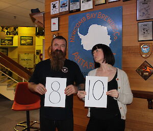 A bearded man and young woman acting as judges hold up signs reading eight and ten