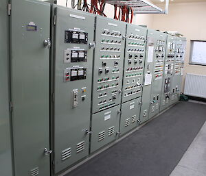 Power house electrical panels lined up against wall on left, with lots of lights and buttons