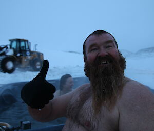 Bearded male expeditioner gives the thumbs up from an outdoor spa in Antarctica.