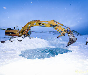 Swim hole being dug out of the ice with a digger.