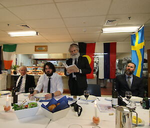 Expeditioner reading during midwinter dinner, standing up at a table.