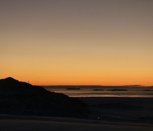 Sunset on midwinter day with a hill to the left, and ice is so dark you can’t make it out, only shadows.