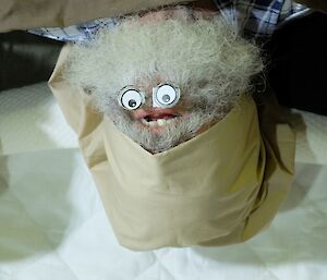 A grey bearded expeditioner poses upside down, with fake eyes in his beard.