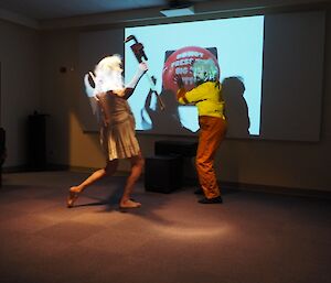 Expeditioners in play entitled Cinderfella, pose as a plumber fairy and title character in front of a projection screen with a large button.