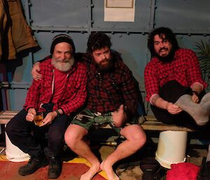 Three male expeditioners enjoy a Friday gathering, sitting on a bench in the tankhouse.