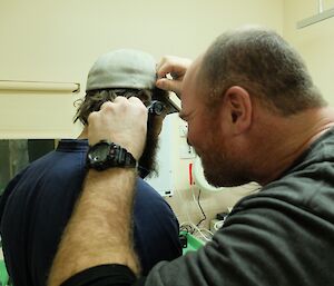 Expeditioner uses a medical instrument to peer inside the ear of another.