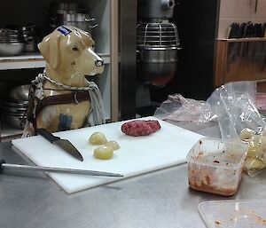 Stay, the plastic mascot dog, posed in kitchen in front of ingredients as if cooking meatloaf.