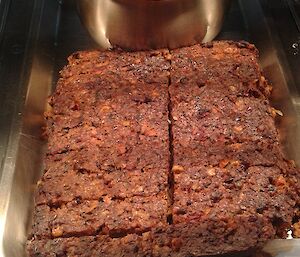 A slab of meatloaf cut into squares is presented in a bain marie, with a pot of tomato based sauce behind it. The name Beatrice is written beneath.