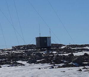 A small hut sits amongst rocks and snow