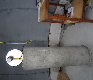 Inside a small hut with tall, thick concrete cylinder with light on top and a small desk on right