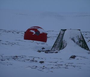 A round hut and small pyramid structure in snow pictured on a heavily overcast day