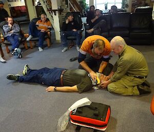 Male expeditioner lies on floor while two others put on his neckbrace