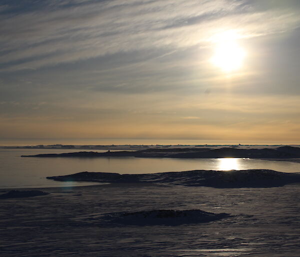 Looking across Shirley Channel and Shirley Island, under a bright sun, slightly hidden by light clouds.