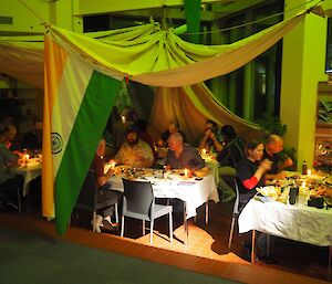 Several tables full of expeditioners sit under a large tent hanging from the ceiling — it features the flag of India.
