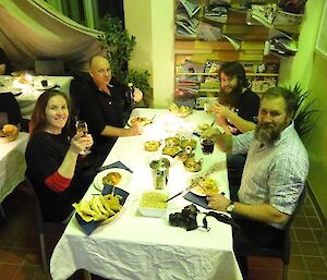 Four expeditioners eating curry sit at a table and toast the camera.