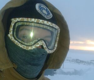 Photo of expeditioner with only eyes visible through goggles — taken outdoors with ice visible in background
