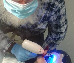 Expeditioner practices dentistry on a dummy while looking up at camera. He wears goggles.