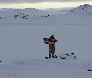 Expeditioner holding the U.S. flag at the Peterson Island Cairn