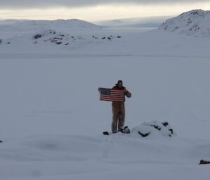 Expeditioner holding the U.S. flag at the Peterson Island Cairn