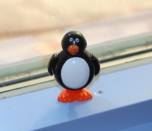 Small plastic toy penguin in window.