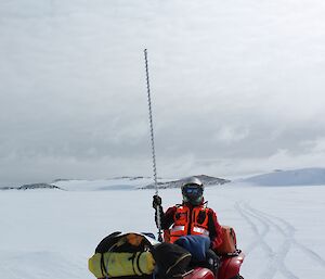 Expeditioner shows how deep the ice is — he is holding a long drill bit while sitting on a quad bike.