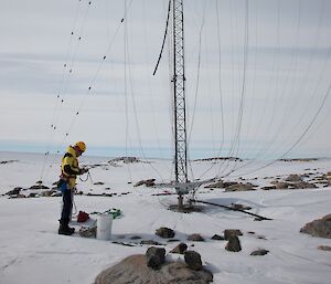 A tall aerial with tentacle-like wires coming down is being looked over by a communications technician