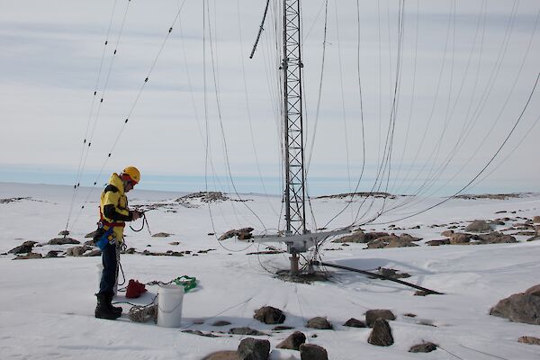 A tall aerial with tentacle-like wires coming down is being looked over by a communications technician