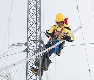Expeditioner at work on a tall metal antenna to which he is harnessed.