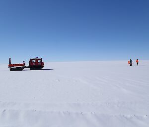A large two cab tracked vehicle on a flat expanse is on the left of the image, while on the far right is two expeditioners dwarfed by the landscape