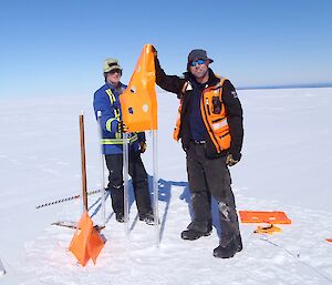 Expeditioners set up flags on the icy ski landing area — the poles as tall as themselves.