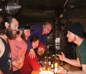 A group of expeditioners in civilian clothing laugh over a candlelit table in a field hut