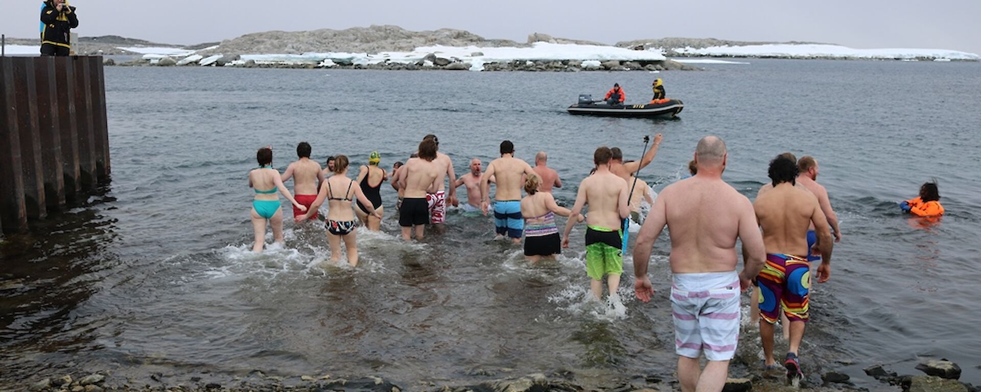 Expeditioners enter water for summer swim, most wearing shoes as the shore is rocky
