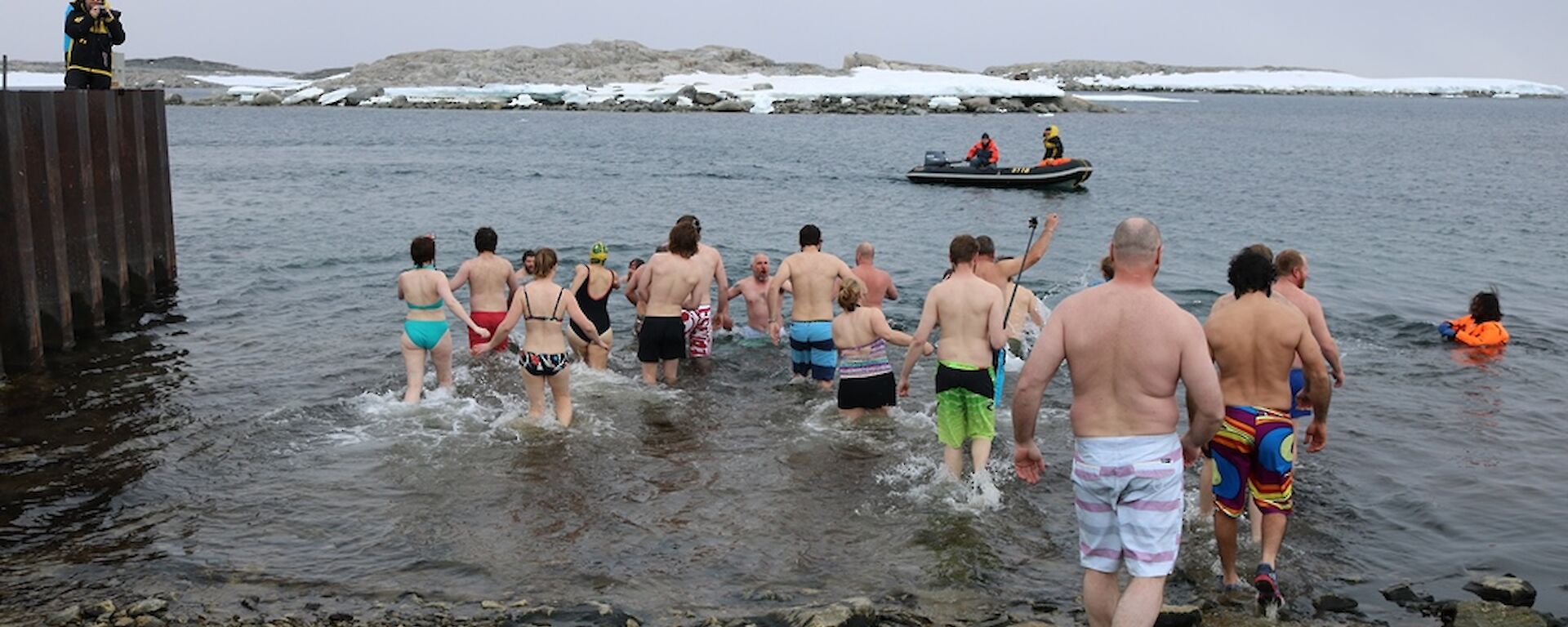 Expeditioners enter water for summer swim, most wearing shoes as the shore is rocky