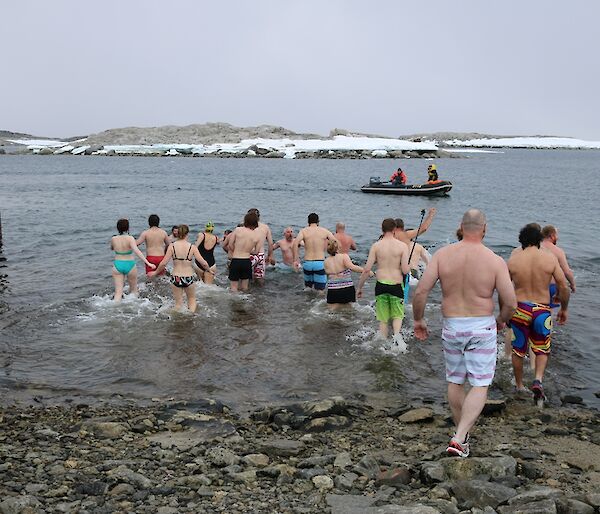 Expeditioners enter water for summer swim, most wearing shoes as the shore is rocky