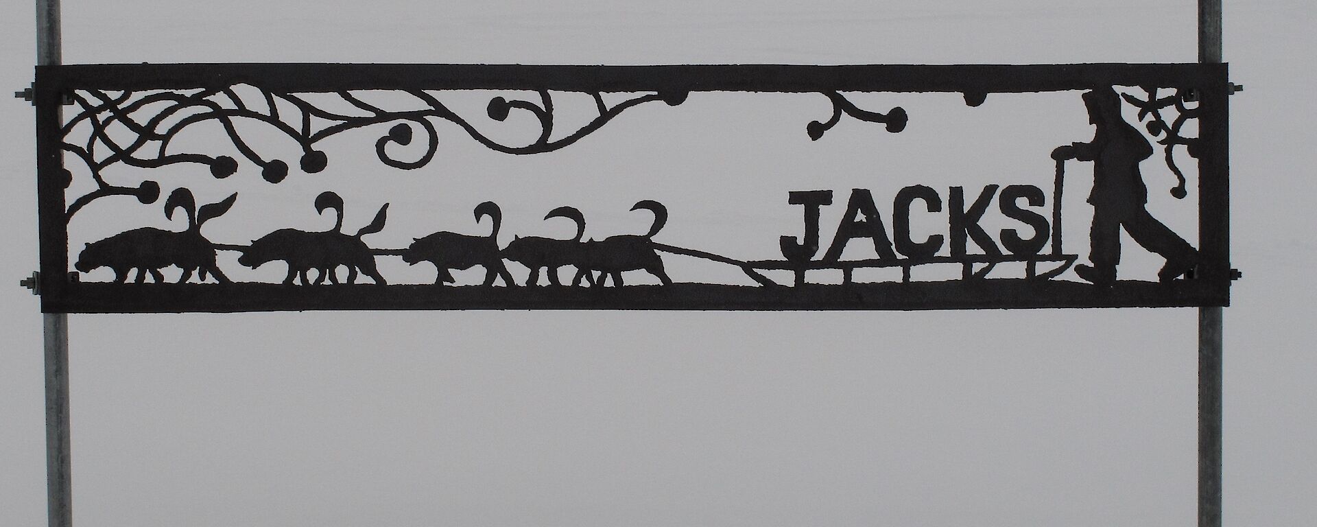 Metalwork sign post that shows a cut out of a man on a sled led by Huskies and the name Jacks