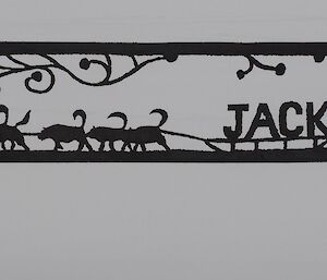 Metalwork sign post that shows a cut out of a man on a sled led by Huskies and the name Jacks