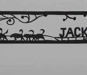 Metalwork sign post that shows a cut out of a man on a sled led by Huskies and the name Jacks