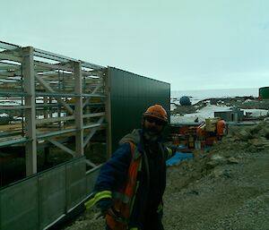 A bearded male expeditioner looks excited as he gestures towards a building being constructed