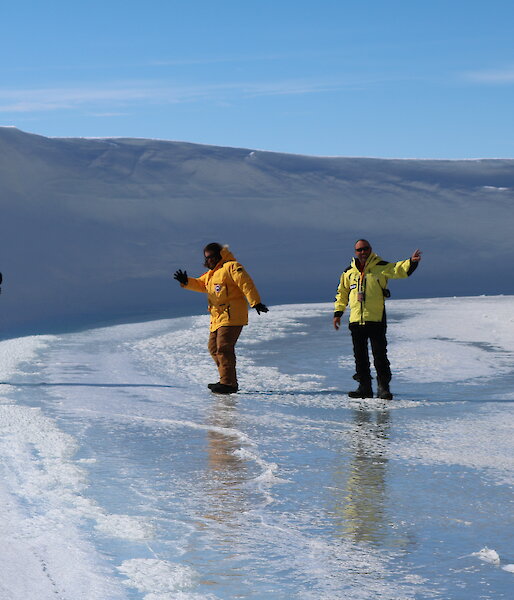 Three male expeditioners standing on ice, one waving to camera