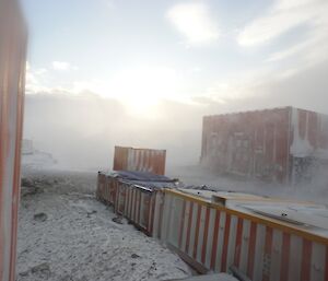 Blizzard blowing between several shipping containers and cargo covered in tarps