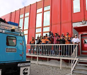 Winter expeditioners standing on the accommodation building deck waving goodbye to the over snow vehicles