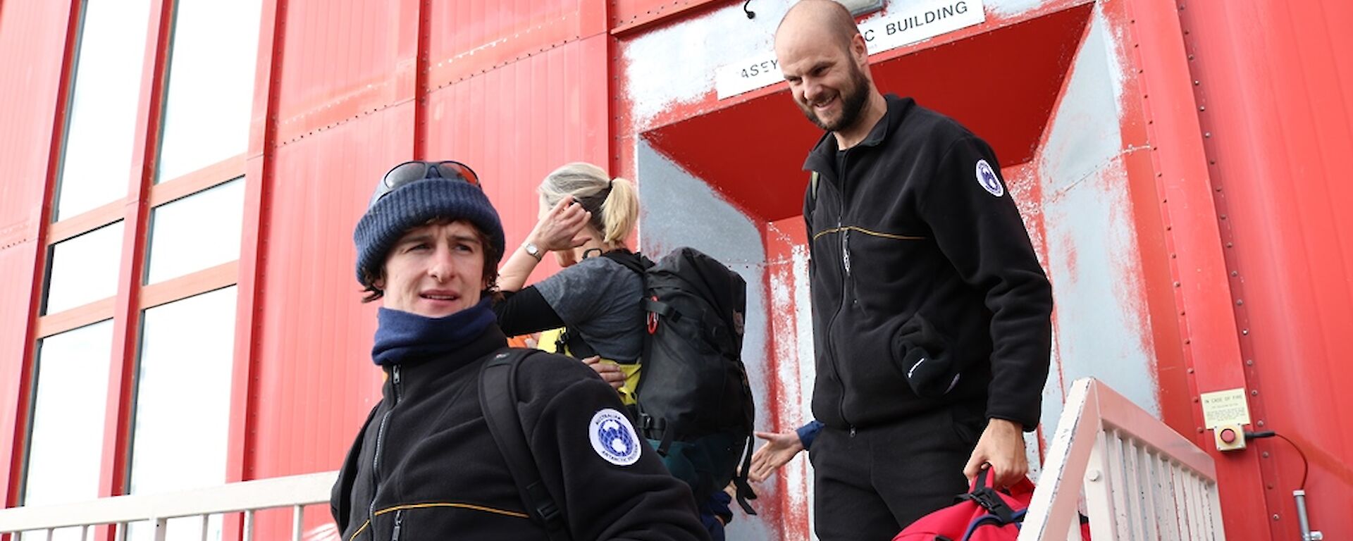Three expeditioners leaving accommodation building to get into over snow vehicles