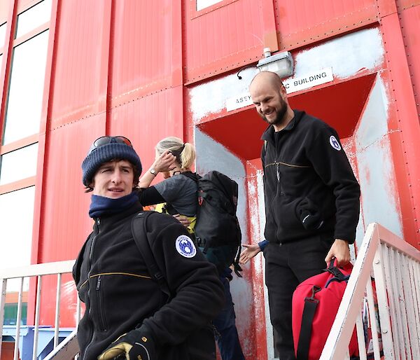 Three expeditioners leaving accommodation building to get into over snow vehicles