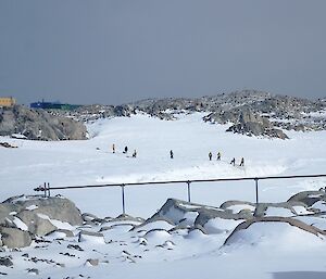 Team of expeditioners training for stretcher rescue on the edge of a crevasse with station buildings in the background.