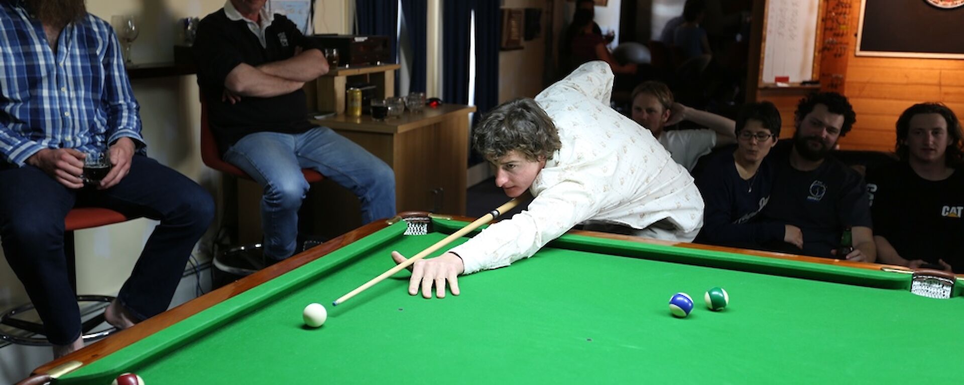 Mark leaning over the pool table to about to play his shot.