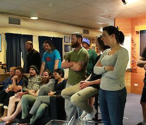 People sitting and standing around the pool table watching the game.