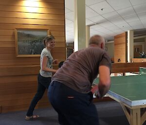 People in action playing a doubles match of table tennis.